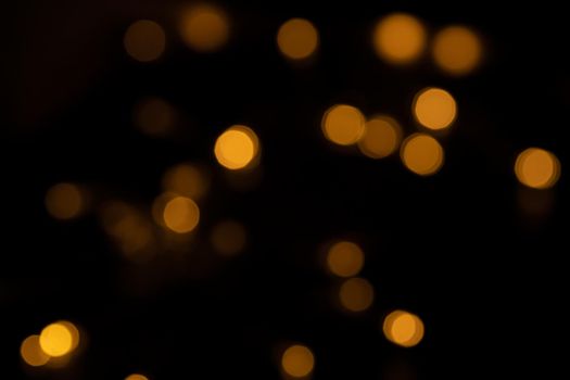 Defocused bokeh lights on black background, an abstract naturally blurred backdrop for Christmas eve or birthday party. Festive light texture. Yellow and red garland in blur. Overlay effect for design