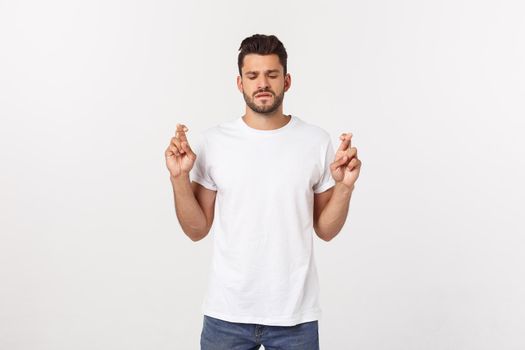 Closeup portrait of young handsome man crossing fingers, wishing, praying for miracle, hoping for the best, isolated on white background