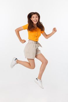 Portrait of a joyful woman jumping in the studio with happy feeling, isolated on white background, 20-28 year old