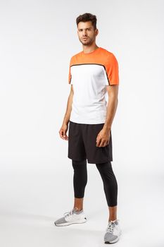 Vertical studio shot male football player in activewear, sneakers standing determined, ready score goal, squinting frowning self-assured, prepare for workout, endurance and sport concept.