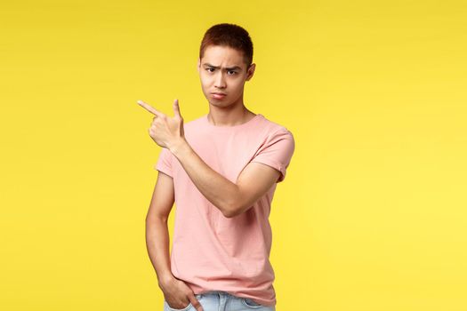 People, different emotions and lifestyle concept. Portrait of gloomy, sad and disappointed asian male pointing finger upper left corner, look angry from under forehead, feel displeased and envy.