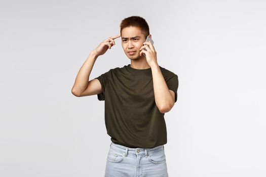 Technology, online lifestyle and communication concept. Portrait of frustrated and confused, judgemental asian guy think speaker is stupid or crazy, talking on phone and cringe displeased.