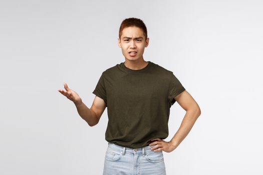So what, why. Portrait of displeased angry asian man look frustrated and bothered, raising hand in dismay and shrugging, dealing with rude person, whats your problem, arguing, grey background.