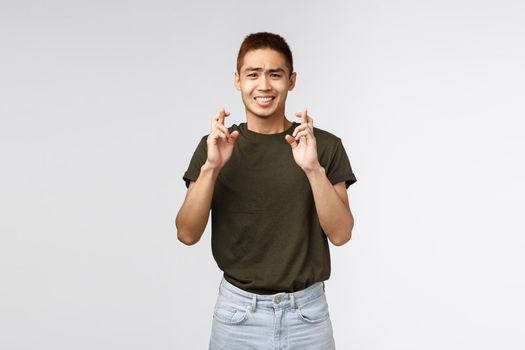 Male student having high hopes about entering university or passing exam. Portrait of happy anticipating man cross fingers for good luck, clenching teeth and look tensed camera.