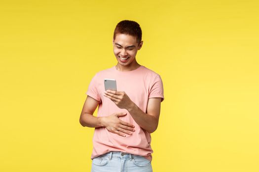 Technology, communication and lifestyle concept. Portrait of happy, enthusiastic asian man laughing at mobile phone screen, smiling pleased, chuckle over funny video online, messaging friends.