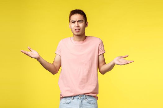 Whats your problem man. Portrait of displeased, frustarted young asian guy look bothered and confused, shrugging, spread hands sideways, cant understand what happened, stand yellow background.