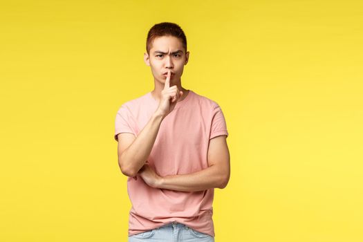 People, different emotions and lifestyle concept. Portrait of displeased asian male student tell to be quiet, shush and dont speak, press index finger to lips and frowning, scolding bad behaviour.
