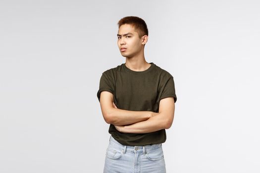 Portrait of suspicious, doubtful asian guy look disbelief camera, squinting staring camera, cross arms chest and frowning, dont trust person, feel hesitant or doubtful, grey background.