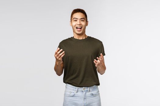 People, emotions and lifestyle concept. Handsome surprised asian guy raising hands up and smiling upbeat as receiving amazing good news, praise friend achievement, look cheerful camera.