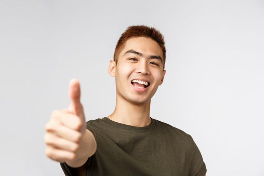 People, different expressions and lifestyle concept. Close-up portrait of upbeat, rejoicing asian man saying yes, show thumb-up in approval, praise nice job, recommend best quality, great deal.