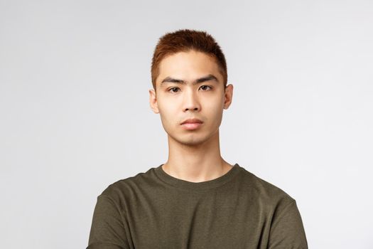 Close-up portrait of serious-looking japanese guy in green t-shirt, look serious and determined, listen to tutor during online lecture while social-distancing at home, standing grey background.