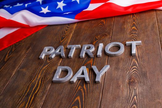 the words patriot day laid with silver metal letters on wooden board surface with crumpled usa flag above in diagonal perspective