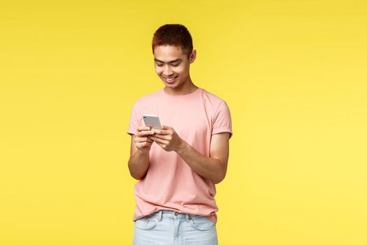 Technology, communication and lifestyle concept. Smiling, enthusiastic handsome asian hipster guy messaging friend, using mobile phone and smiling at smartphone display pleased, texting.