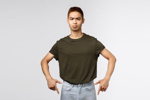 Serious-looking annoyed and disappointed young asian man complaining or scolding person, frowning and look camera with dismay and irritation, pointing fingers down angry. Copy space