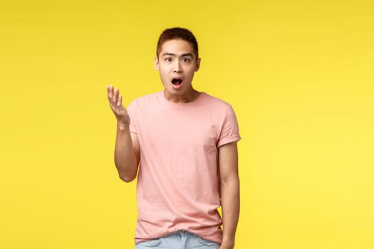 People, different emotions and lifestyle concept. Shocked, surprised and impressed asian male in pink t-shirt, stylish haircut, raise hand up and look astounded at camera, open mouth fascinated.