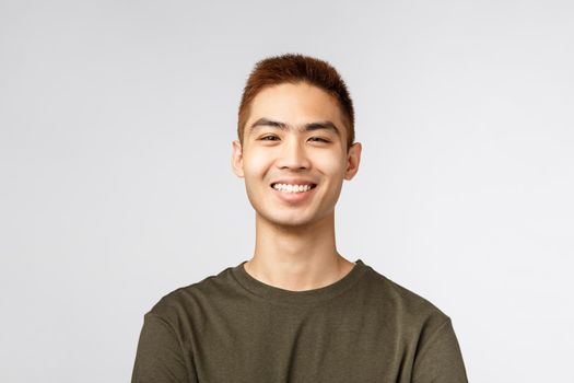 Close-up portrait of satisfied, cheerful nice young male student, asian man look enthusiastic with beaming smile, feeling rejoice and upbeat feeling, standing grey background joyful.