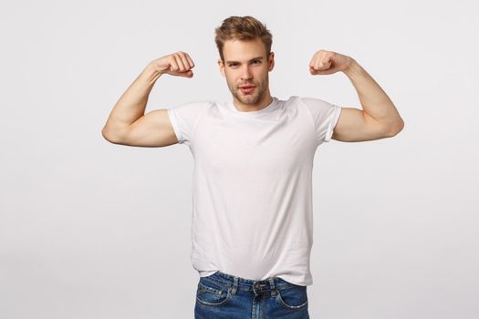 Masculine confident and sassy blond bearded caucasian man, standing white background with flexed biceps, be in good shape, workout and bragging, being boastful own body shape or strength.