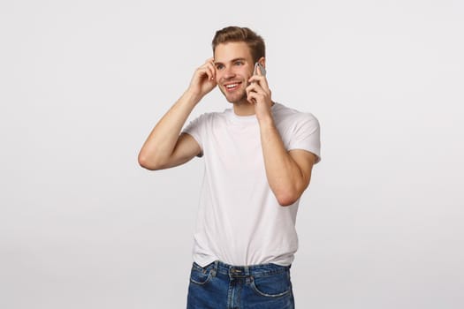 Enthusiastic and curious, carefree smiling blond caucasian guy have interesting conversation, got call from employee, receive good news, holding smartphone near ear, talking phone, touching ear.