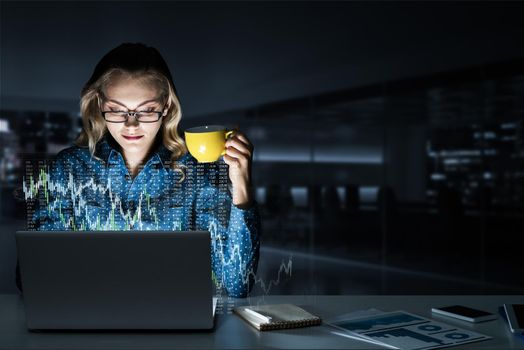 Attractive woman looking at her laptop screen sitting in night office. Mixed media