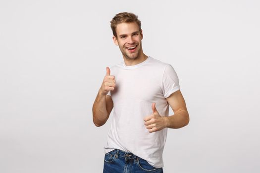 Joyful, charismatic blond bearded guy in white t-shirt, showing thumbs-up and dancing from satisfaction, delight, hear interesting idea, accept plan, agree with friend, give approval, like gesture.