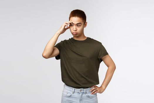 Annoyed and distressed, tensed asian guy facepalm, sighing irritated, look away trying avoid eye contact in awkward moment, dont like person, strange person approaching, grey background.