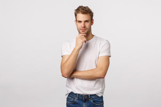 Hmm interesting. Handsome blond guy involved in conversation, discuss with friend open own IT company, touch chin and smiling pleased, agree with partner, have thoughts, white background.