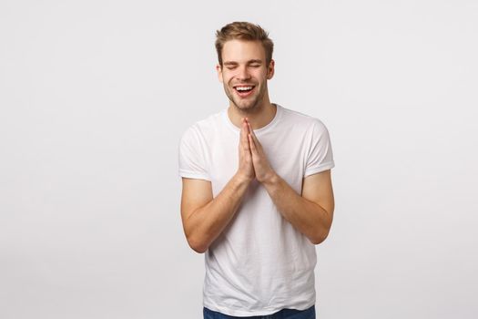 Dreamy and hopeful lucky blond guy feeling fortune near, press hands pray, anticipating relish, hoping achieve success, smiling and close eyes supplication, asking god fulfill dream, white background.