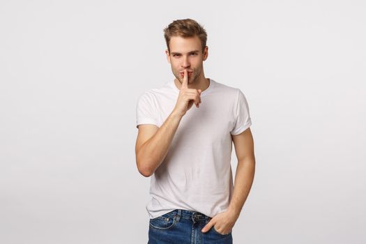 Sensual and creative, charming mysterious handsome blond man prepare secret for girlfriend, want make surprise, shushing with flirty smile, look camera, press index finger to lips, hush gesture.