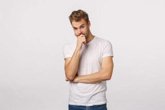 Troubled and shocked, indecisive blond handsome boyfriend, dont know what do, facing difficult problem, look away nervous and distressed, losing patience temper, touch lips, stand white background.