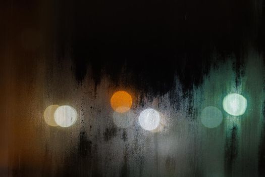 dirty foggy night window glass texture with blurred street lights in the background.