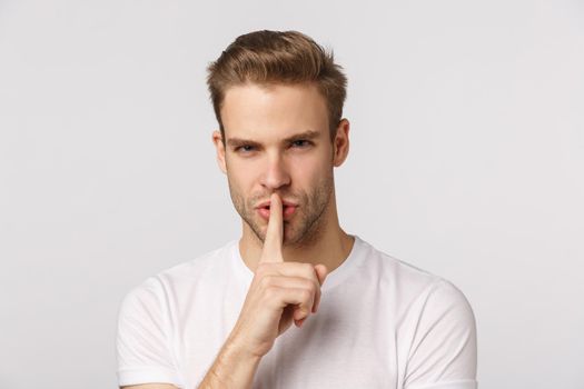 Close-up studio portrait blond handsome, sassy bearded guy squinting displeased, look strict and bossy, shushing, press index finger to lip telling be quiet, stay silent, keep secret, hushing.