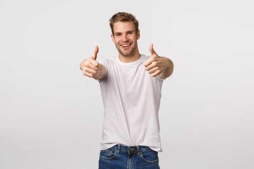 Optimistic and upbeat good-looking blond caucasian guy with bristle, extend hands with thumbs-up to praise friend, congratulate with win, good effort, think product excellent, give approval.