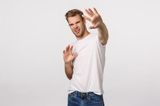 Turn-off that light. Displeased and bothered young handsome man defending himself trying cover something bright with raised hands, squinting discomfort, grimacing, famous person avoiding paparazzi.