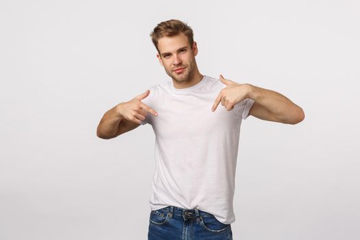 I am all you need. Handsome, assertive male model promote himself, pointing chest and smiling self-assured, want participate, suggest own candidature, standing white background.