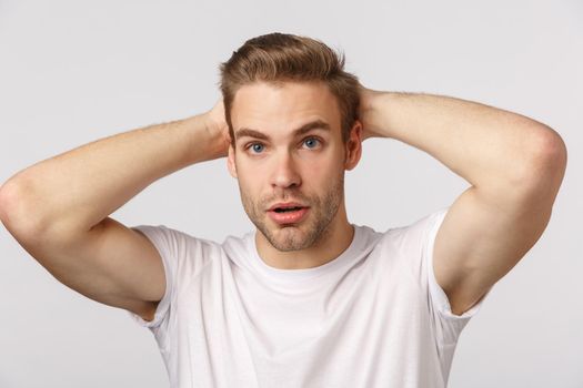 Concerned and troubled, nervous young handsome blond guy, feel anxious before important interview or casting, hold hands behind head, look indecisive, standing white background.