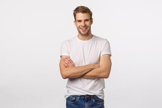 Enthusiastic, happy smiling blond man with bristle, white t-shirt, jeans, cross arms chest and grinning amused, hear interesting story, accepting good idea, agree with person, white background.