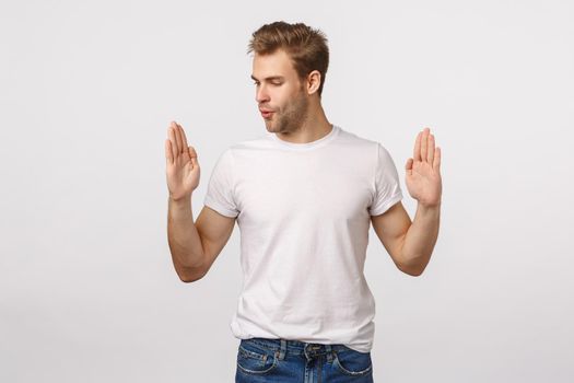 Handsome blond young man amazed with size of product as if holding something large or big, shaping object and observe it, wistle from amazement being impressed, white background.