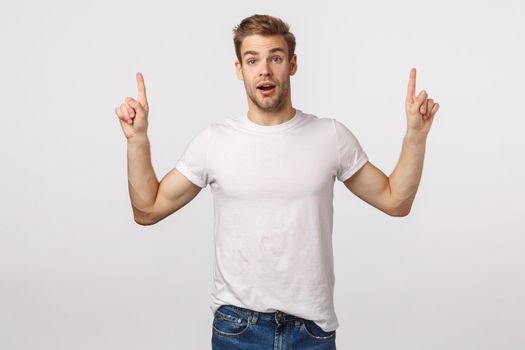 You certainly need download it. Amuased attractive and excited, astounded blond cute bearded man in white t-shirt, pointing fingers up, gasping astonished, speechless, see something interesting.