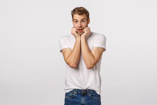 Tender and cute charming silly blond guy with bristle, feeling amused or express fascinated, look touched, press hands to cheeks lovely, gasping stare with admiration or temptation, white background.