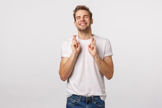 Pretty please god make my dream come true. Cute lucky and hopeful charming blond guy making wish, cross fingers good luck, smiling and raise head up sky, relish good news, white background.