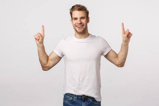 Dreamy delighted good-looking blond bearded man in white t-shirt, pointing fingers up and smiling impressed, being uplifted, have inspiration from attending awesome event, recommend.