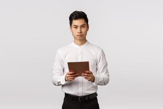 Business, finance and recruitment concept. Handsome elegant young asian man holding digital tablet and looking camera serious, being busy, control work remote, hr interviewing applicants.