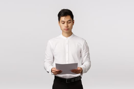 Business, corporate economy and people concept. Serious-looking busy elegant asian male entrepreneur holding documents, reading paper, prepare for office meeting, studying financial report.