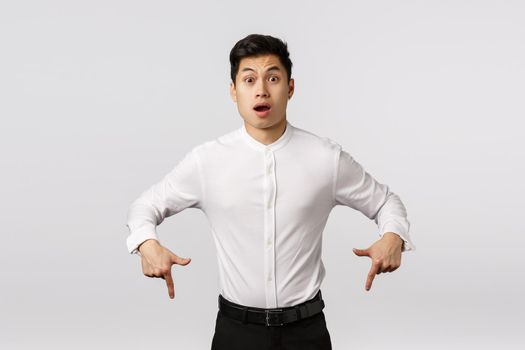 Freak out, alarmed and surprised shocked asian handsome guy in collar shirt, pants, pointing down, gasping amazed and speechless, say wow, hear strange unexpected news, white background.