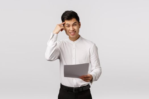 Are you out of your mind. Displeased, angry asian male entrepreneur pointing at temples, frowning disappointed, holding documents, read something stupid or strange, scolding coworker.