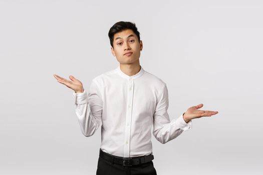 Well sorry but that it. Attractive asian male coworker dont know how help, shrugging and spread hands sideways, grimacing puzzled, cant answer, have no idea, standing clueless white background.