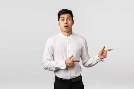 Shocked, freak out concerned cute asian boyfriend hear girlfriend pregnant, gasing shook and astonished, standing speechless open mouth amazement, pointing right indecisive, white background.