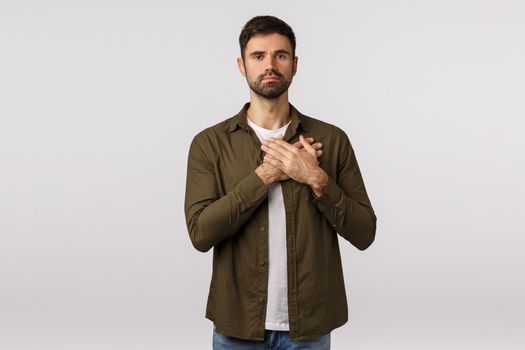 Devoted and courageous, dedicated young bearded man, press hands on heart and look camera, express loyalty and faith, listen national anthem, feeling moved or touched, white background.