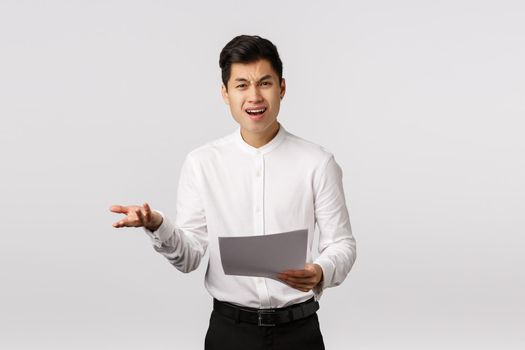 What the heck. Displeased, angry and furious young asian businessman receive bad report, raise hand in dismay, frowning, look frustrated and disappointed, holding papers, read bad document.