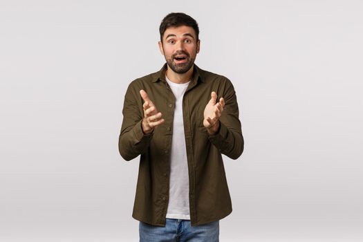 Cheerful and relieved happy surprised young kind bearded man, describe his impressions and amazement, gesturing with hands as having conversation, smiling joyful, standing white background.